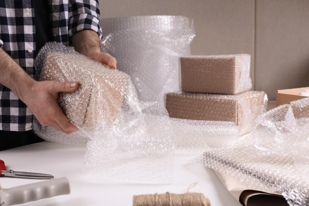 Man,Covering,Box,With,Bubble,Wrap,At,Table,In,Warehouse,